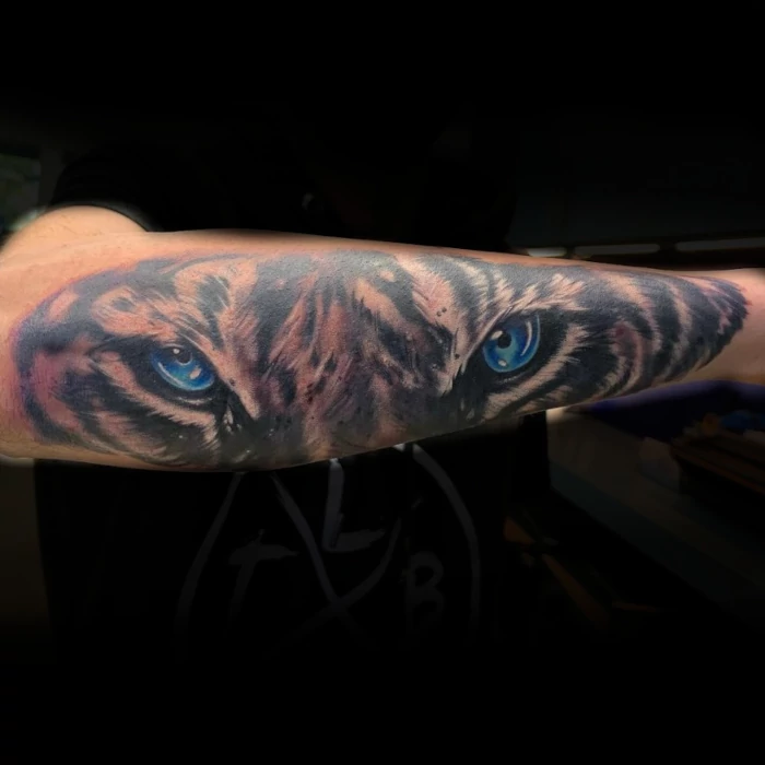 Fine line black and grey tiger head forearm tattoo with blue eyes by Sacred Mandala tattoo artist Russ Howie in Durham, NC.